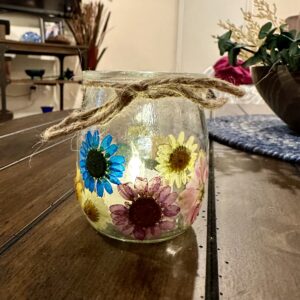 glass jar covered with dried pressed flowers on a rustic wood table