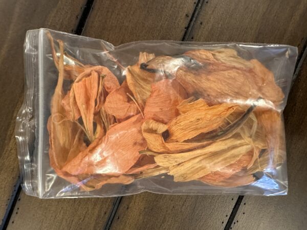 a clear pouch of orange lily dried flower petals on a rustic brown table