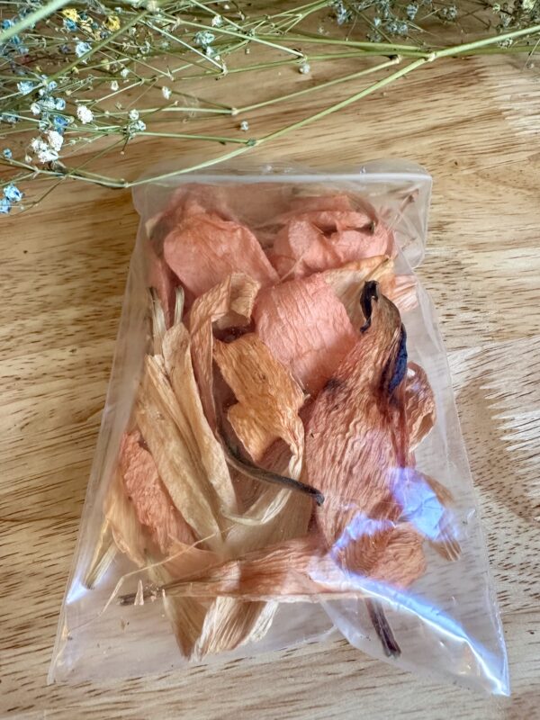 a clear pouch of orange lily dried flower petals on a wood background next to some dried flowers