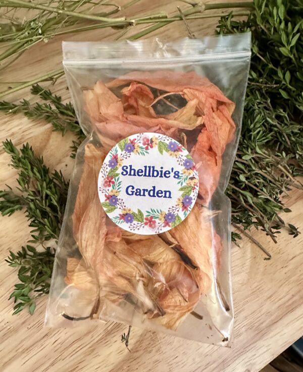 a clear pouch of orange lily dried flower petals laying on top of dried herbs with a label that says shellbies garden