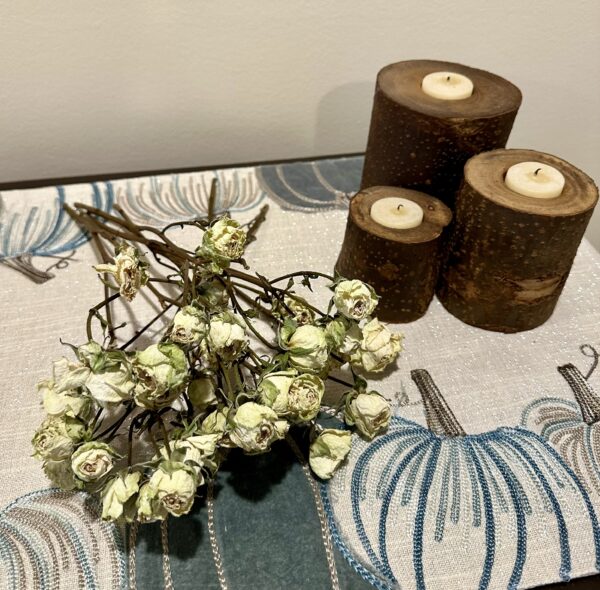 mini white dried roses on a white and blue cloth table with tree trunk candle holders