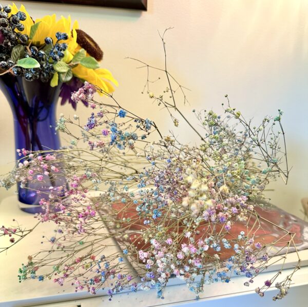 pink, blue, and white babys breath flower stems laying next to a blue glass vase